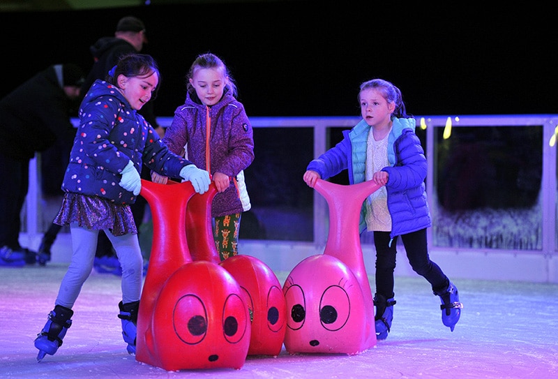 Children ice skating together on the Winter Glow ice rink using beluga whale skate aids.