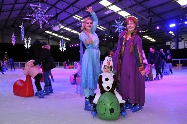 Ice Princesses Elsa and Anna posing on the ice rink with a child.