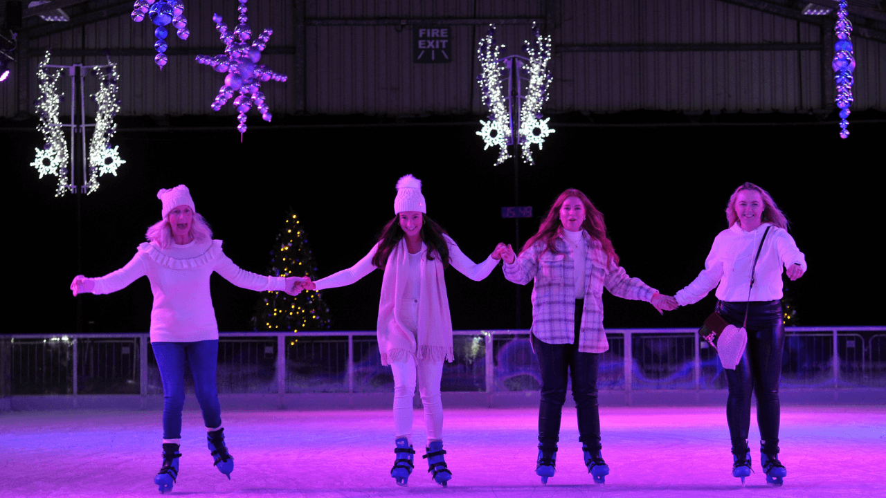 four women holding hands ice skating on the ice rink at Winter Glow.