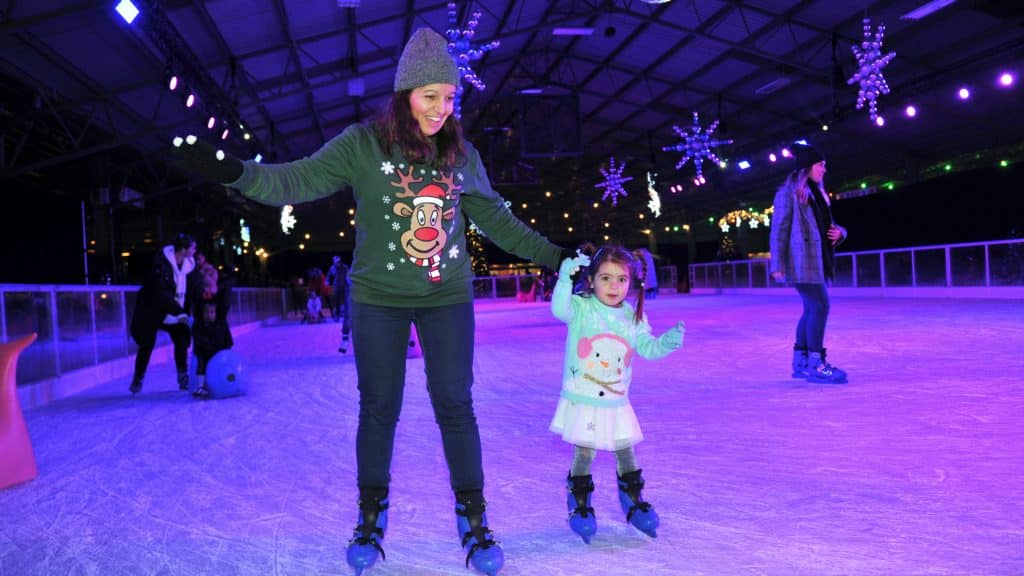 A woman and her daughter holding hands ice skating on the Winter Glow ice rink.