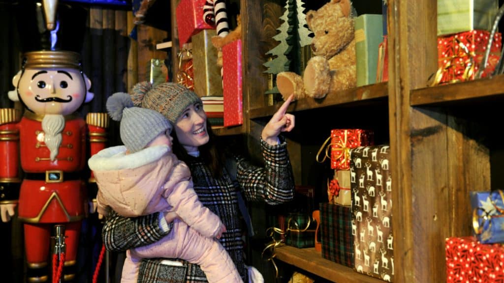 A woman holding her baby and pointing to toys on the shelf in the Toy Workshop at Winter Glow.