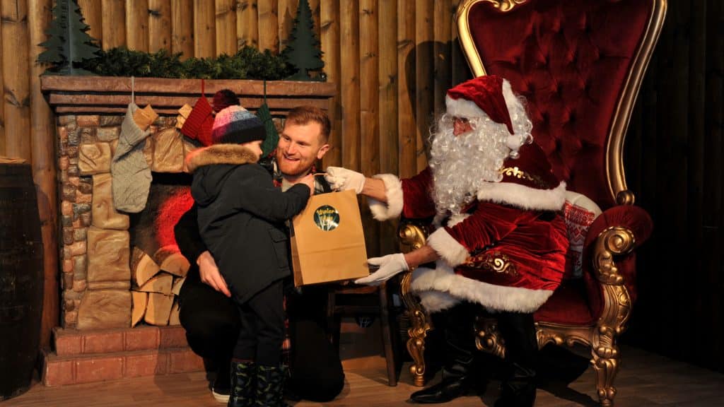 A father and his child meeting Santa at the Personalised Santa Experience with Santa handing the child a gift.