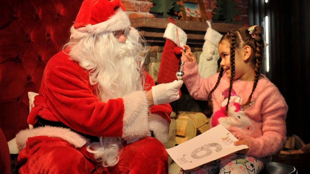 A young girl meeting with Santa, with Santa handing her a gift.
