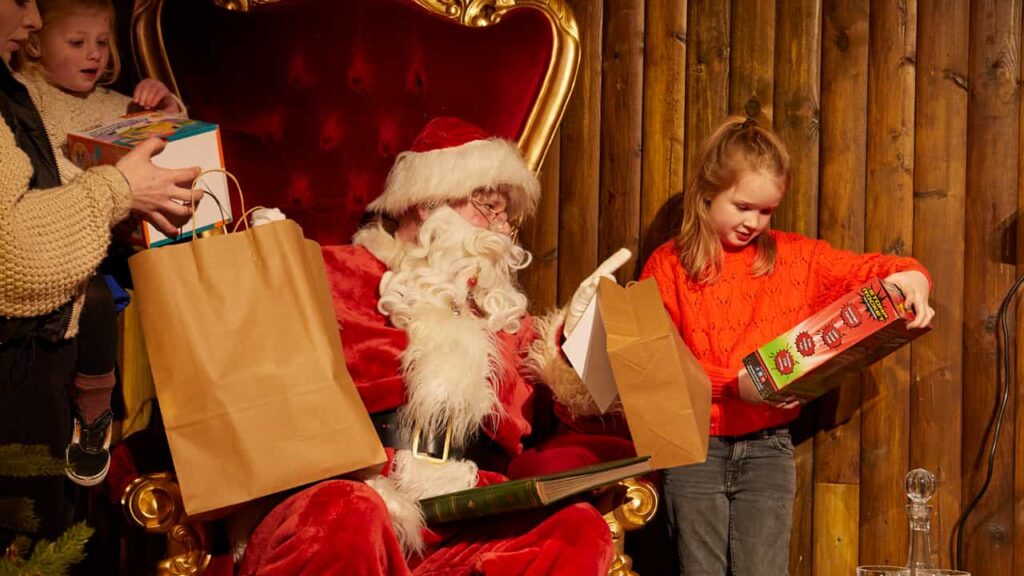 Child holding a present with Santa Claus next to her, watching.